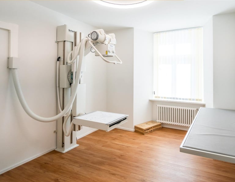 Medical X-ray room with radiograph equipment, examination table, and wooden flooring in a bright clinical setting