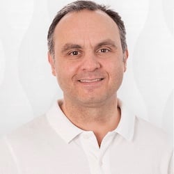 Professional headshot of a middle-aged man with short gray hair wearing a white collared shirt against a neutral background