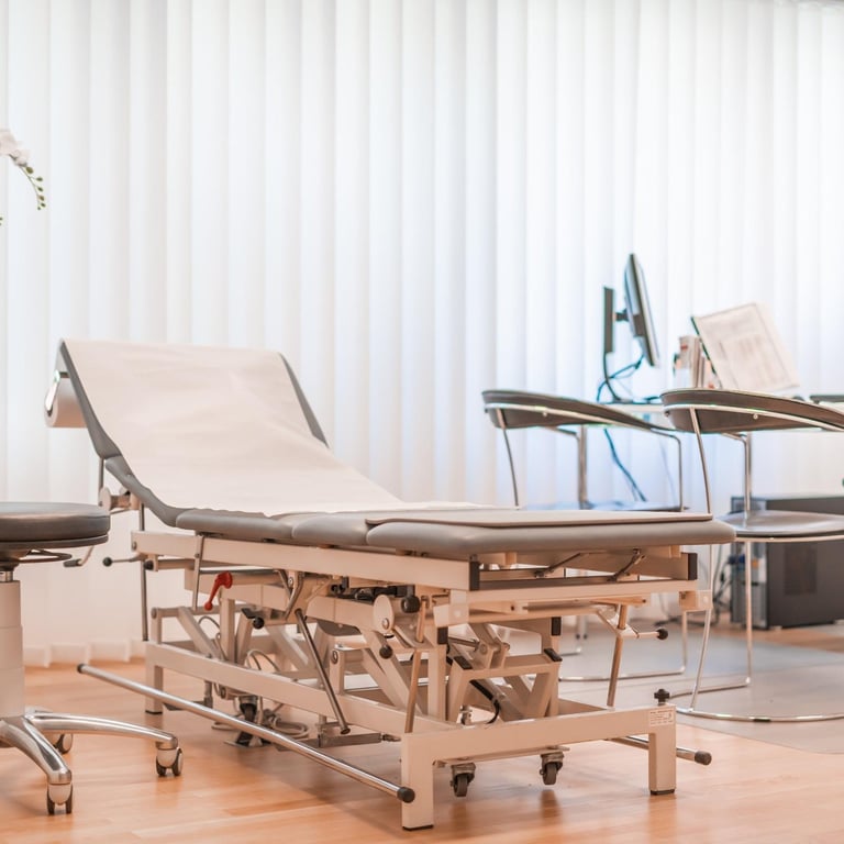 Medical examination bed with hydraulic adjustable height frame on wheels in a clinical room with white curtains